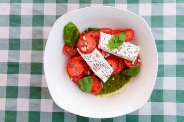 Çilekli Caprese salatası, mozzarelller, fesleğen ve balzamik sos yeşil ekose arka planda beyaz bir kasede servis edilir. İtalyan mutfağı konsepti, yaz menüsü, geleneksel çilekli tarifi..