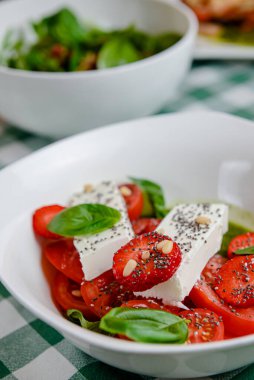 Çilekli Caprese salatası, mozzarelller, fesleğen ve balzamik sos yeşil ekose arka planda beyaz bir kasede servis edilir. İtalyan mutfağı konsepti, yaz menüsü, geleneksel çilekli tarifi..