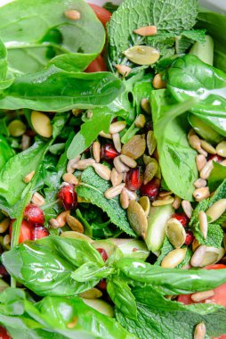 Domatesli ıspanak salatası, taze roka, kabak çekirdeği, yeşil ekoseli beyaz bir kasede servis edilen nar tohumları. İtalyan mutfağı kavramı.