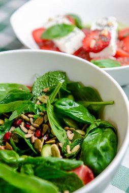 Domatesli ıspanak salatası, taze roka, kabak çekirdeği, yeşil ekoseli beyaz bir kasede servis edilen nar tohumları. İtalyan mutfağı kavramı.