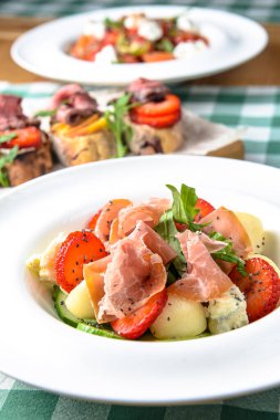 Çilekli salata, prosciutto, otlar, süzme peynir ve beyaz tabakta hazırlanmış böğürtlen sirkesi. Yeşil ekose arka planda. İtalyan mutfağı kavramı.