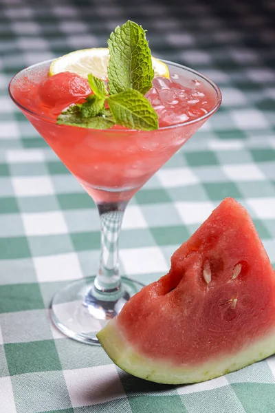 Water melon cocktail and fresh melon, on a table with green plaid tablecloth. Summer drink, cold beverage for hot summer weather.