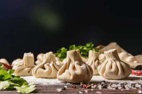 Gürcü köftesi ya da Khinkali. Ahşap arka planda ev yapımı Gürcistan Khinkalisi. Yan görüş, seçici odaklanma. Taze yeşillik, baharat ve çiğ mantarla.
