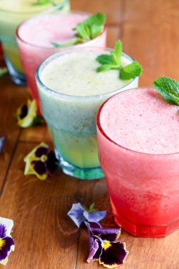 Lezzetli sağlıklı kivi ve çilekli meyve püresi, ahududu püresi. Kırsal ahşap masada taze nane şekeriyle servis ediliyor. Soğuk yaz taze içkileri.