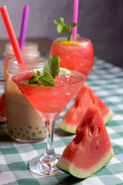 Water melon cocktails and fresh melon, on a table with green plaid tablecloth. Summer drink, cold beverage for hot summer weather.