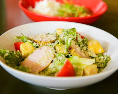 Sezar Salatası, restoranda ya da lokantada masada beyaz bir kasede servis edilir. Sezar salatasının geleneksel tarifi, seçici odaklanma, bulanık arkaplan.