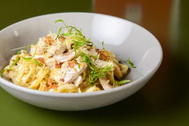 Peynirli, soslu İtalyan tortellini makarnası ve beyaz bir kasede servis edilen mikroyeşillikler. İtalyan mutfağı kavramı, geleneksel makarna tarifi.