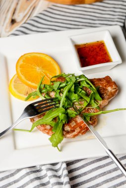 Taze yeşil roka, portakal dilimleri ve domates sosuyla servis edilmiş ızgara biftek. Beyaz bir tabakta. İtalyan mutfağı kavramı.