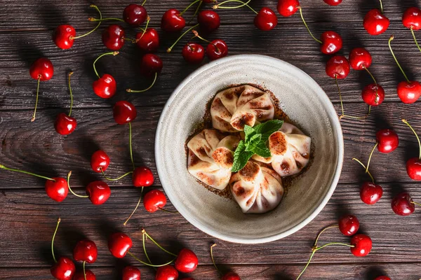 伝統的なグルジア料理とアルメニア料理 白いプレートに桜とグルジアのキンカリ 木製のテーブルの上に 選択的フォーカス ボウルに甘い桜団子 素朴なスタイル 新鮮な桜の周り ロイヤリティフリーのストック画像