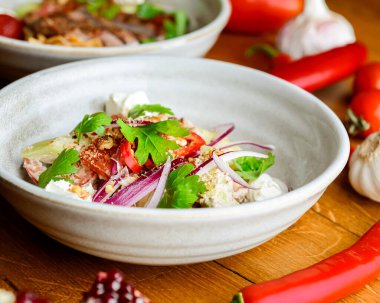 Domatesli salata, peynir ve tatlı ve ekşi soslu kişniş. Gürcistan mutfağı. Sağlıklı yiyecekler. Kırsal ahşap masada diğer tabaklarla birlikte bir kasede servis edilmiş..