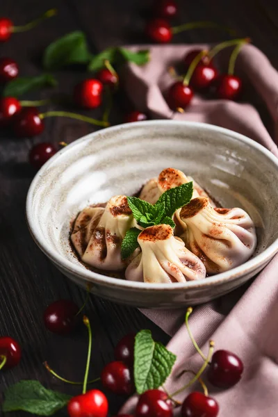 伝統的なグルジア料理とアルメニア料理 白いプレートに桜とグルジアのキンカリ 木製のテーブルの上に 選択的フォーカス ボウルに甘い桜団子 素朴なスタイル 新鮮な桜の周り ストックフォト