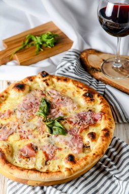 Kırsal ahşap masada pizza dilimlenmiş bir bardak kırmızı şarap. İtalyan mutfağı kavramı, jambonlu ve peynirli pizza, beyaz arka plan..