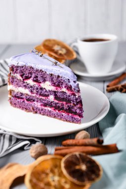 Beyaz bir tabakta lavantalı kek kes. Ahşap zemin üzerinde beyaz bir tabakta servis edilen lavanta ve böğürtlenli mor menekşe pastası. Çay saati için lezzetli tatlı..