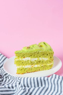 Fıstıklı pasta, beyaz tabakta fındıklı kremalı pasta. Fıstıklı tatlı pasta. Pastel pembe arka planda yeşil tatlı. Arka planda bir fincan kahve ve lavantalı kek..