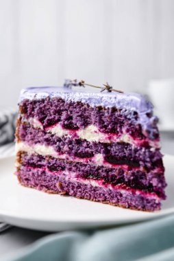 Beyaz bir tabakta lavantalı kek kes. Ahşap zemin üzerinde beyaz bir tabakta servis edilen lavanta ve böğürtlenli mor menekşe pastası. Çay saati için lezzetli tatlı..