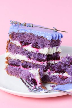 Beyaz bir tabakta lavantalı kek kes. Pembe arka planda beyaz bir tabakta servis edilen lavantalı ve dutlu mor menekşe pastası. Çay saati için lezzetli tatlı..