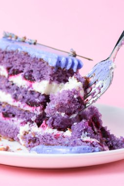 Beyaz bir tabakta lavantalı kek kes. Pembe arka planda beyaz bir tabakta servis edilen lavantalı ve dutlu mor menekşe pastası. Çay saati için lezzetli tatlı..