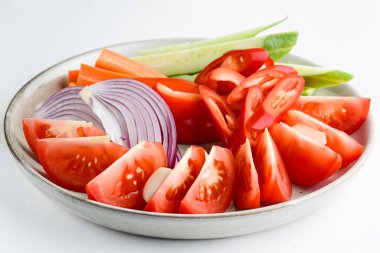 Beyaz arka planda izole edilmiş seramik tabakta gökkuşağı renginde sebzeler kes. Domates, salatalık, biber, soğan. Öğle yemeği fikri..