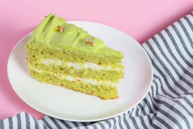 Fıstıklı pasta, beyaz tabakta fındıklı kremalı pasta. Fıstıklı tatlı pasta. Pastel pembe arka planda yeşil tatlı. Arka planda bir fincan kahve ve lavantalı kek..