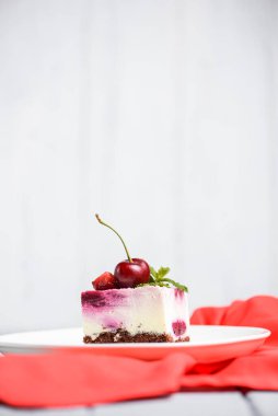 Beyaz arka planda beyaz bir tabakta servis edilen üzerinde krema ve taze kirazlı gül kirazlı cheesecake. Lezzetli tatlı zamanı, pastayı kapat, uzay afişini kopyala.