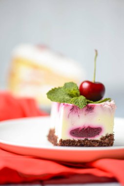 Beyaz arka planda beyaz bir tabakta servis edilen üzerinde krema ve taze kirazlı gül kirazlı cheesecake. Lezzetli tatlı zamanı, pastayı kapat, uzay afişini kopyala.