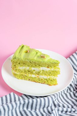 Fıstıklı pasta, beyaz tabakta fındıklı kremalı pasta. Fıstıklı tatlı pasta. Pastel pembe arka planda yeşil tatlı. Arka planda bir fincan kahve ve lavantalı kek..
