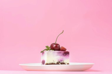 Kremalı ve taze vişneli gül vişneli kek üzerine beyaz bir tabakta servis edilmiş pastel pembe arka plan. Lezzetli tatlı zamanı, pastayı kapat, uzay afişini kopyala.