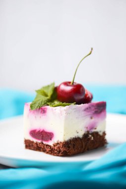 Beyaz arka planda beyaz bir tabakta servis edilen üzerinde krema ve taze kirazlı gül kirazlı cheesecake. Lezzetli tatlı zamanı, pastayı kapat, uzay afişini kopyala.