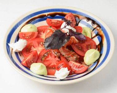 Beyaz arka planda beyaz tabakta servis edilen fesleğenli geleneksel Caprese Salatası. Beyazda izole edilmiş. İtalyan mutfağı konservesi. Geleneksel tarif.