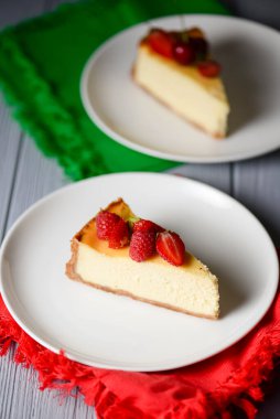 Lezzetli bir parça New York usulü vanilyalı cheesecake. Üstünde böğürtlen var. Beyaz tabakta servis edilmiş, seçici bir odak noktası. Geleneksel New York Cheesecake tarifi. Hafif ahşap arkaplanda.