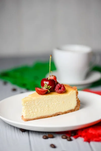おいしいニューヨークスタイルのバニラチーズケーキの上に果実が付いています 白いプレート 選択的な焦点で提供しています ニューヨークチーズケーキの伝統的なレシピ 薄木を背景に ロイヤリティフリーのストック写真
