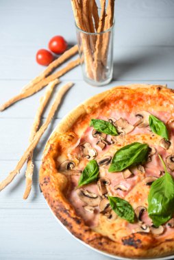 Mantarlı iştah açıcı pizza ve hafif ahşap arka planda taze fesleğen. İtalyan mutfağı kavramı, taze pişmiş pizza.