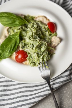 Ispanaklı Tagliatelle makarnası, vişneli domates, tavuk ve taze fesleğen. Masada beyaz bir tabakta servis edilmiş. İtalyan mutfağı kavramı, geleneksel makarna tarifi.