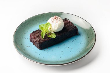 Beyaza izole edilmiş mavi bir tabakta servis edilen dondurmalı çürümüş browni. Vanilyalı dondurmalı çikolatalı tatlı. Geleneksel browni tarifi.