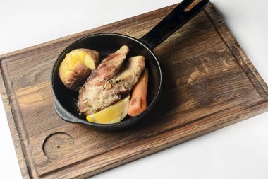 Limon dilimli ızgara somon, fırında patates ve havuç, beyaz arka planda kırsal ahşap bir tahtada kızartma tavasında servis ediliyor. Ukrayna mutfağı kavramı.