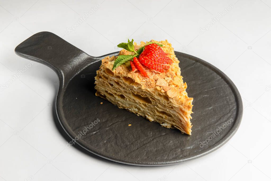 Cake Napoleon with fresh strawberry on top served on a black plate isolated on a white background. Traditional recipe of cake Napoleon dessert.