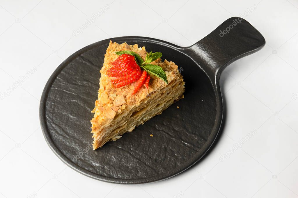 Cake Napoleon with fresh strawberry on top served on a black plate isolated on a white background. Traditional recipe of cake Napoleon dessert.