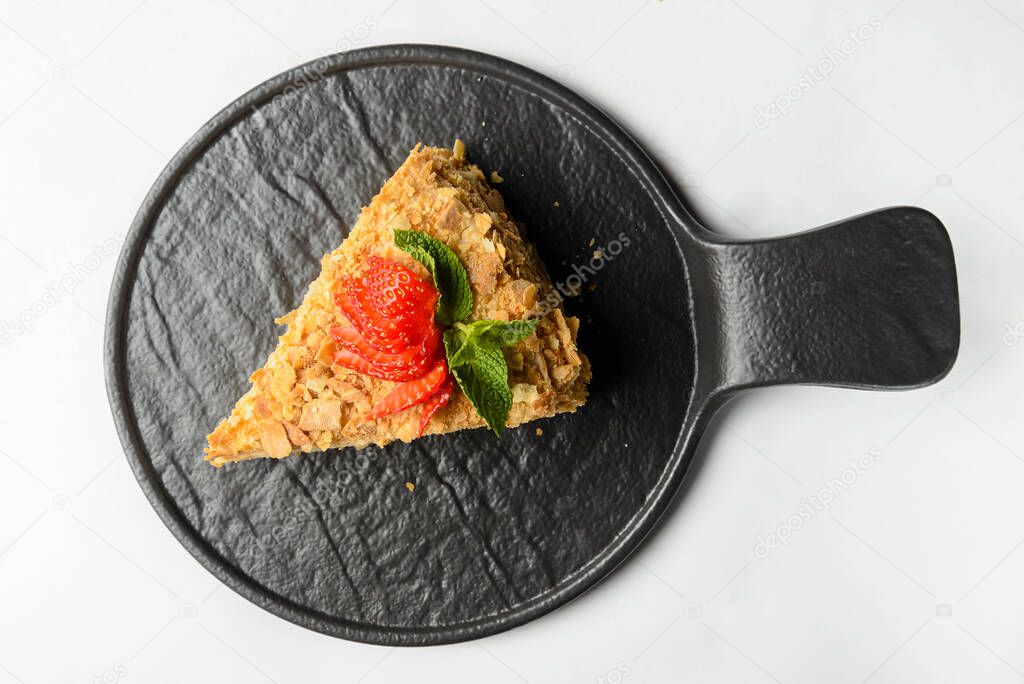 Cake Napoleon with fresh strawberry on top served on a black plate isolated on a white background. Traditional recipe of cake Napoleon dessert.