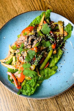 Mavi bir tabakta servis edilen taze sebzeli kuşkonmaz ve susam tohumlu salata karışımı. Öğlen ya da akşam yemeği fikri, sağlıklı yemek..