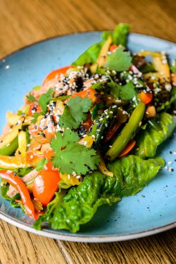 Mavi bir tabakta servis edilen taze sebzeli kuşkonmaz ve susam tohumlu salata karışımı. Öğlen ya da akşam yemeği fikri, sağlıklı yemek..