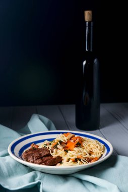 Biftek, sebze, sarımsak ve taze biberiyeli sade spagetti. İtalyan yemeği. İtalyan mutfağı. Lezzetli ve sağlıklı bir yemek için konsept. Koyu ahşap arka planda bir şişe şarapla.