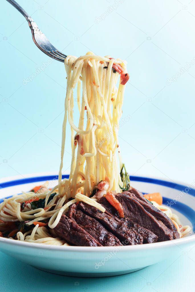 Closeup of rustic spaghetti with beefsteak, vegetables, garlic and fresh rosemary. Italian food. Italian cuisine. Concept for a tasty and hearty dish. Over blue background.