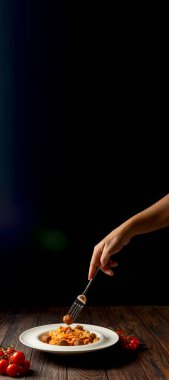 Siyah arka planda beyaz tabakta servis edilen köfteli spagetti. İtalyan mutfağı konsepti. Uzay afişini kopyala. Elleri çatalla yiyecek arıyor..