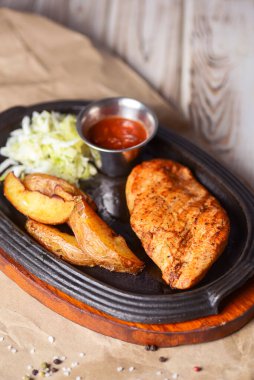 Kızarmış Rus patatesli ızgara tavuk fileto bifteği, yeşil salata ve domates sosu kırsal ahşap arka planda servis edilir. Akşam yemeği..