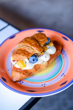 İçinde krem peynir ve yaban mersini bulunan lezzetli kruvasanlar bir restoranın içindeki renkli bir tabakta servis ediliyor. Arka plan bulanık. Lezzetli tatlı kahvaltı.