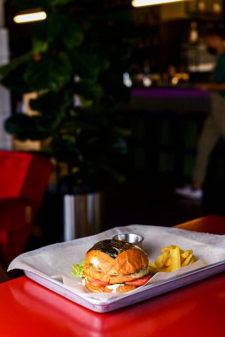 Bir restoranın içindeki kırmızı masada metal tepside servis edilen patatesli hamburger. Fast food, abur cubur kavramı.