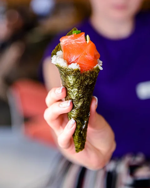 Japan sushi roll in womans hand inside a restaurant. Creative idea for a sushi roll. Roll with rice and salmon fish inside.