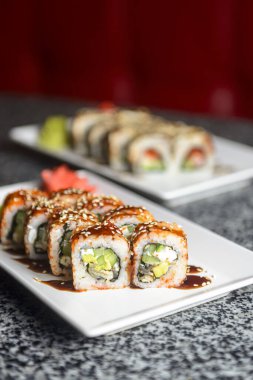 Avokado ve krem peynirli Philadelphia ya da California suşisi. Suşi menüsü. Geleneksel Japon yemeği konsepti. Restoranda beyaz bir tabakta servis edilir, konsepti dışarıda yenir..