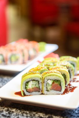 Philadelphia ya da California avokado ve krem peynirli suşi sarar. Yeşil ejderha suşisi. Geleneksel Japon yemeği konsepti. Restoranda beyaz bir tabakta servis edilir, konsepti dışarıda yenir..