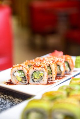 Avokado ve krem peynirli Philadelphia ya da California suşisi. Suşi menüsü. Geleneksel Japon yemeği konsepti. Restoranda beyaz bir tabakta servis edilir, konsepti dışarıda yenir..